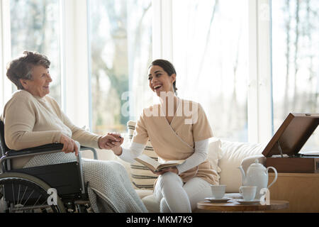 Gute Beziehung zwischen lächelnden Krankenschwester und glücklich behinderte ältere Frau im Pflegeheim Stockfoto