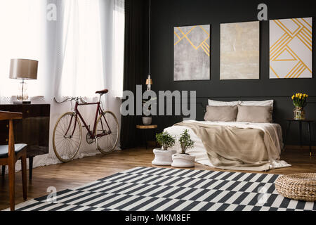 Modernes Schlafzimmer Innenraum mit schwarze Wand, mit dem Fahrrad durch das Fenster, Lampe, Stuhl, Hocker, Pflanzen, Bildern und Teppichen Stockfoto