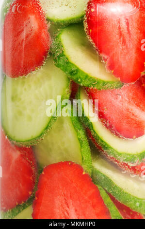 Erdbeeren und Gurken schwimmen in das glitzernde Wasser. Hausgemachte Limonade aus Erdbeeren und Gurken. Fruchtschnitten in Wasser mit Luftblasen. Stockfoto