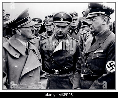 HITLER, HIMMLER, HENLEIN, Vintage WW2 1940 B&W-Bild von Adolf Hitler, Führer der Nazipartei (Nationsozialistische Deutsche Arbeiterpartei; NSDAP), Bundeskanzler von 1933 bis 1945 und Führer („Führer“) von Nazideutschland von 1934 bis 1945 Heinrich Himmler Reichsführer des Schutzpersonels (Schutzschwadron; Waffen SS) und ein führendes Mitglied der Nazi-Partei (NSDAP) des Deutschen und Konrad Henlein Reichsstatthalter und Gauleiter des Reichsgau Sudetenland mit einem Hakenkreuz-Armband. Alle in Uniform stehen und reden, mit SS-Offizieren, die sich hinter ihnen befinden Stockfoto