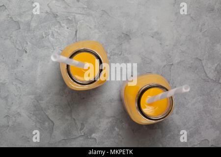Orangensaft in einer Glasflasche auf grauem Hintergrund. Ansicht von oben Stockfoto