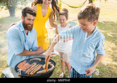 Vater und Sohn die Zubereitung von Fleisch auf Holzkohle Grill während Picknick Stockfoto