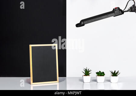 Holzrahmen mit schwarzen Platz für Text. Mock up. Stilvolle Inneneinrichtung. Grüne Pflanze in einem weißen Topf auf Schwarz-weiße Wand im Hintergrund Stockfoto