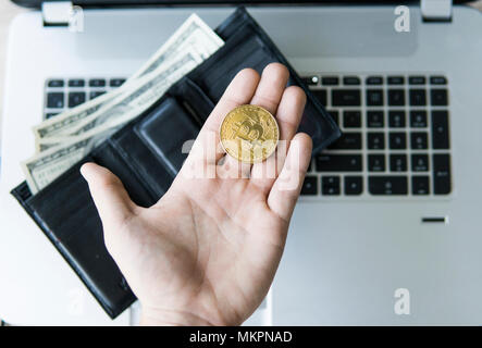 Golden bitcoin Münze in der Hand des Menschen mit einem Laptop auf Hintergrund und Leder Geldbörse mit Geld. Mann hält eine crypto Währung in der Hand. Virtuelles Geld. Bu Stockfoto