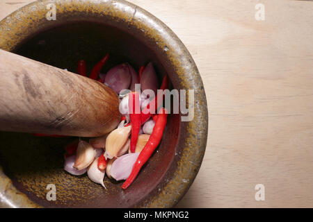 Im Mörser mit Pistill, Knoblauch, Schalotten, roter Chili. Alle auf einem Holzbrett. Stockfoto