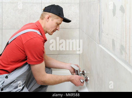 Klempner Holding eine Badewanne Armatur und installiert es. Stockfoto