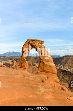 Sonnenuntergang am Zarten Arch - Vertikal - Bunte Zarten Arch im hellen Abendsonne, mit Rolling Rocky Mountains im Hintergrund, Arches National Park. Stockfoto