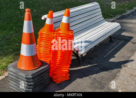 Viele orange road Leitkegel im Freien und weißen Bank im Stadtpark. Sicherheit Zeichen verwendet, um Unfälle beim Straßenbau zu verhindern. Stockfoto