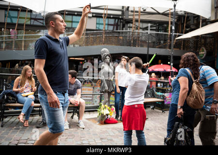 Mit dem Handy filmt Man Camden Stables Market; Bronzestatue von Amy Winehouse und Menschen herumlaufen Stockfoto