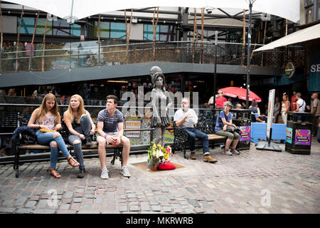 Leute sitzen auf den Bänken neben der Bronzestatue des späten Sängerin Amy Winehouse im Camden Stables Markt in Camden Town, London, UK. Stockfoto