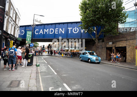 Blaue Taxi fährt durch Chalk Farm Road vorbei an der Camden Town Eisenbahnbrücke in Camden Town, London, UK. Stockfoto