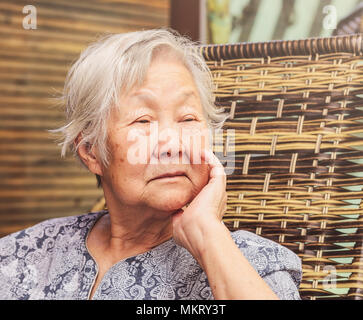Einsame alte Dame zu Hause sitzt, mit der Hand am Kinn mit einem traurigen Gesichtsausdruck. Stockfoto