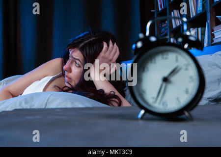 Foto der unglückliche Frau mit Schlaflosigkeit liegend auf Bett neben Wecker Stockfoto