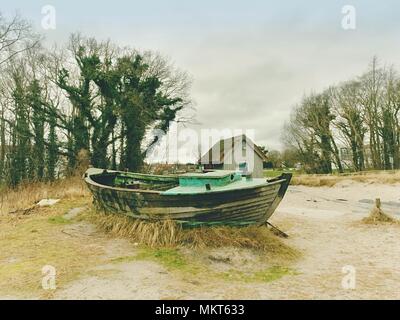 Abgebrochene Fischerboot auf Bank von Meer. Morgen stille Bucht innerhalb windstill. Dramatische und malerische Szene. Dark Sky in Wasser spiegel Stockfoto