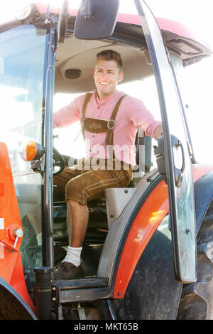 Schöne blonde bayerische Mann sitzt auf Traktor Stockfoto