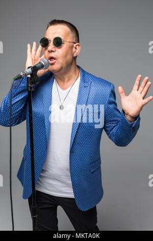 Das mittlere Alter Showman Interviewer mit Emotionen. Junge elegante reifer Mann mit Mikrofon gegen den weißen Hintergrund. Stockfoto