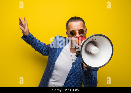 Reifer Mann in Sonnenbrille sprechen mit Lautsprecher auf gelbem Hintergrund Stockfoto