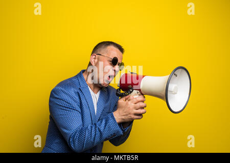 Reifer Mann in Sonnenbrille sprechen mit Lautsprecher auf gelbem Hintergrund Stockfoto