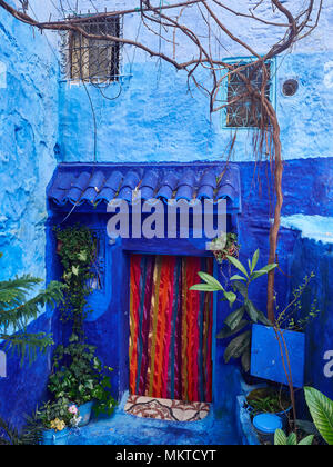 Helle rote Vorhänge in einem quadratischen Fenster auf einer blauen Wand, Chefchaouen, Marokko. Stockfoto