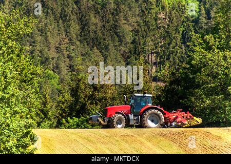 Feld und den Betrieb des Traktors. Wind und Staub über Arbeiter. Rote Traktor auf dem Feld. Landwirtschaftliche Landschaft in der Tschechischen Republik Stockfoto