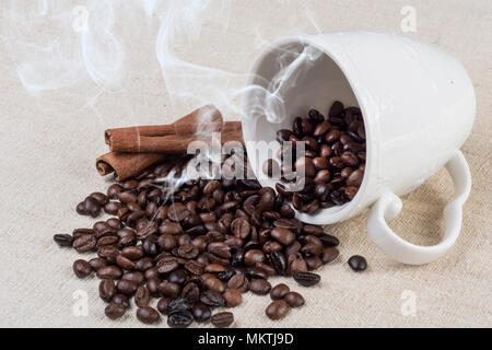 Frisch gerösteten Kaffee Bohne rauch und aus der Tasse Kaffee und Zimt auf retro Schreibtisch verschüttet. Close Up, selektiver Fokus Stockfoto