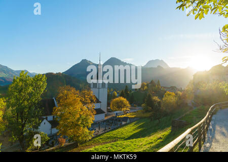 Landschaft mit einer traditionellen Kirche in den nebligen Strahlen der untergehenden Sonne und Wald, Bulle, Schweiz Stockfoto