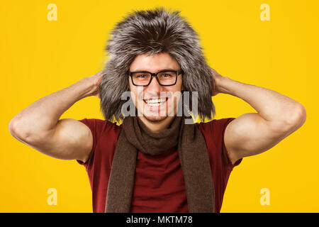 Fröhliche stattlicher Mann mit stilvollen furry Hut und Brille in die Kamera lächeln auf gelben Hintergrund. Stockfoto