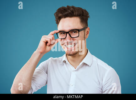 Glückliche junge Mann mit weißem Hemd und Brille auf blauem Hintergrund posiert Stockfoto