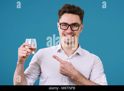 Fröhlicher schöner Mann in Brillen und Holding Glas mit erfrischenden Drink auf es auf blauem Hintergrund. Stockfoto
