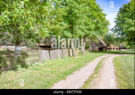 Eine Landstraße in einer alten traditionellen polnischen Dorf mit reetgedeckten Häuser, Bäume und Zäune. Stockfoto