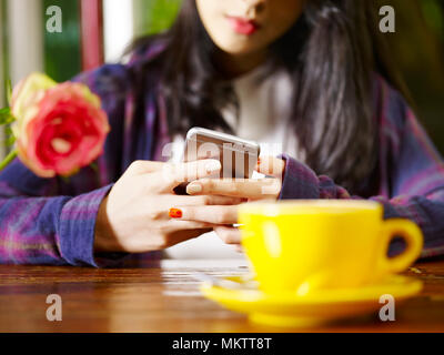 Asiatische Frau spielen mit Handy beim Trinken von Kaffee Cappuccino, auf Händen konzentrieren. Stockfoto