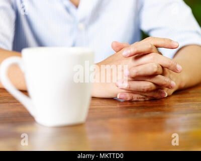 Hände von einem jungen Mann und einer weißen Becher auf hölzernen Tisch im Café oder Tee Haus. Stockfoto