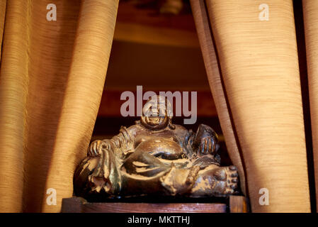 Eine alte Statuette close-up auf einer hölzernen Oberfläche auf beiden Seiten des Vorhangs. Talisman Hotei von Feng Shui ist der Gott des Glücks, Kommunikation, Spaß und Stockfoto