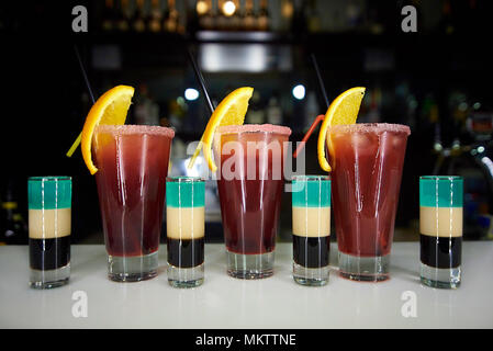 Mehrfarbige Schüsse und Cocktails auf einer Theke vor einem dunklen Hintergrund. Stockfoto