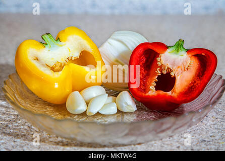 Zwei Paprika und Zwiebeln und Knoblauch liegen auf der Glasplatte auf dem Tisch in der Küche Stockfoto