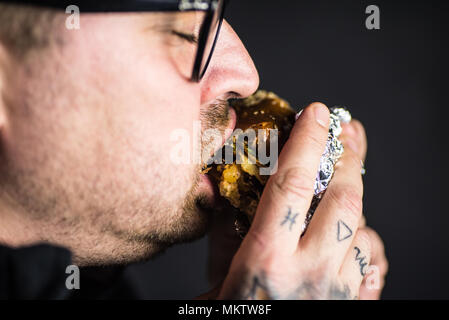 Mann Essen einer frischen, hausgemachten Burger auf einem schwarzen Hintergrund. Anschauliche redaktionelle Inhalte. Stockfoto