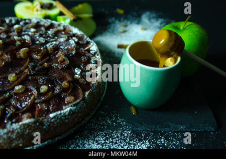 Apfelkuchen mit Karamell Sahne auf Schwarzer Tisch mit Zucker im Hintergrund und Apple Stockfoto