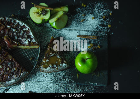 Apfelkuchen mit Karamell Sahne auf Schwarzer Tisch mit Zucker im Hintergrund und Apple Stockfoto