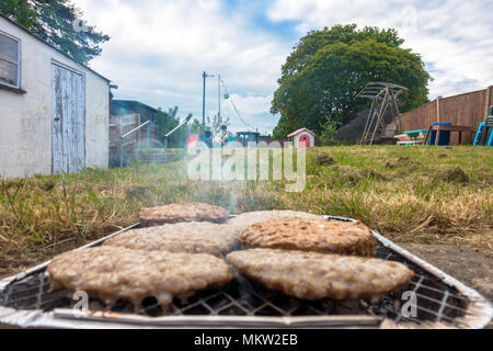 Eine Nahaufnahme der Burger Kochen mit Einweg Grill in einem ruhigen Garten. Stockfoto