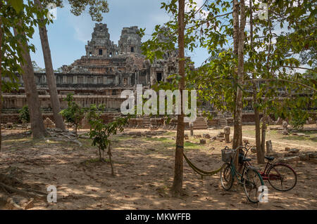 Von Bäumen im Vordergrund schattiert, zwei Fahrräder stehen vor Ta Keo Tempel warten auf die Besucher. Stockfoto