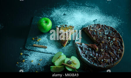 Apfelkuchen mit Karamell Sahne auf Schwarzer Tisch mit Zucker im Hintergrund und Apple Stockfoto