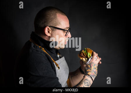 Mann Essen einer frischen, hausgemachten Burger auf einem schwarzen Hintergrund. Anschauliche redaktionelle Inhalte. Stockfoto