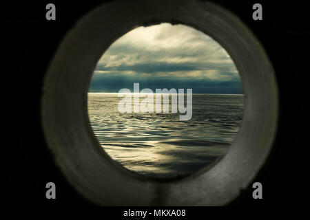 Schiff Fenster oder Bullauge Ansicht mit einer entspannenden Marine und dunkelgraue Wolken Stockfoto