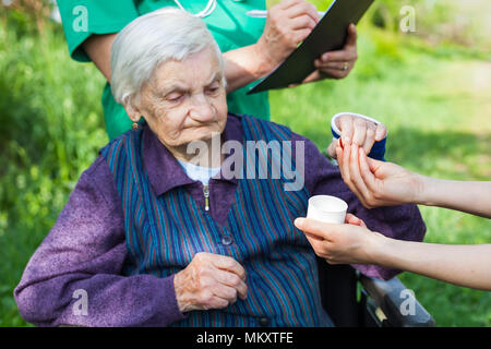 Ältere kranke Frau, die Pillen von Krankenschwester outdoor, Arzt schreiben ärztliche Verschreibung im Hintergrund Stockfoto