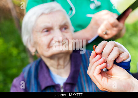 Ältere kranke Frau, die Pillen von Krankenschwester outdoor, Arzt schreiben ärztliche Verschreibung im Hintergrund Stockfoto