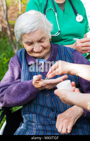 Ältere kranke Frau, die Pillen von Krankenschwester outdoor, Arzt schreiben ärztliche Verschreibung im Hintergrund Stockfoto
