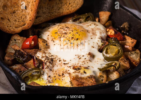 Breakfrast hash in Gusseisen Skillet mit sunny side up gebratene Eier, Schinken, Pilze, würzige Paprika, Kartoffeln, Toast und Kaffee. Stockfoto