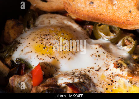 Breakfrast hash in Gusseisen Skillet mit sunny side up gebratene Eier, Schinken, Pilze, würzige Paprika, Kartoffeln, Toast und Kaffee. Stockfoto