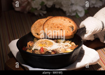 Breakfrast hash in Gusseisen Skillet mit sunny side up gebratene Eier, Schinken, Pilze, würzige Paprika, Kartoffeln, Toast und Kaffee. Stockfoto