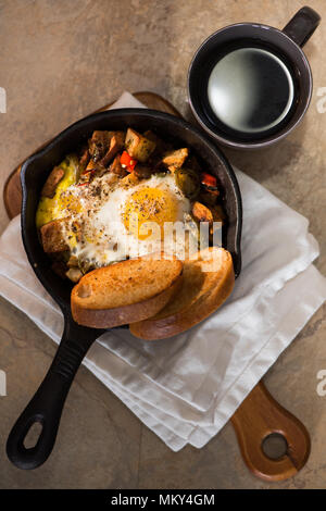 Breakfrast hash in Gusseisen Skillet mit sunny side up gebratene Eier, Schinken, Pilze, würzige Paprika, Kartoffeln, Toast und Kaffee. Stockfoto